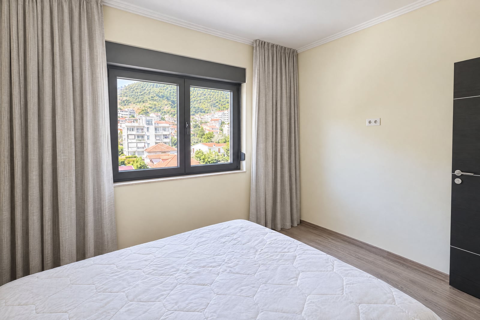 Bright bedroom with a bed and a window overlooking the mountains and the city in Budva, Montenegro
