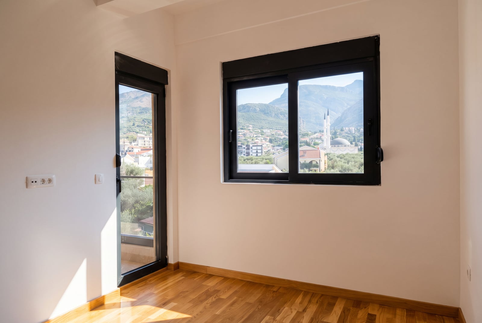 Bright bedroom with parquet flooring and balcony access in an apartment in the city of Bar, Montenegro, with views of the mountains and the city.