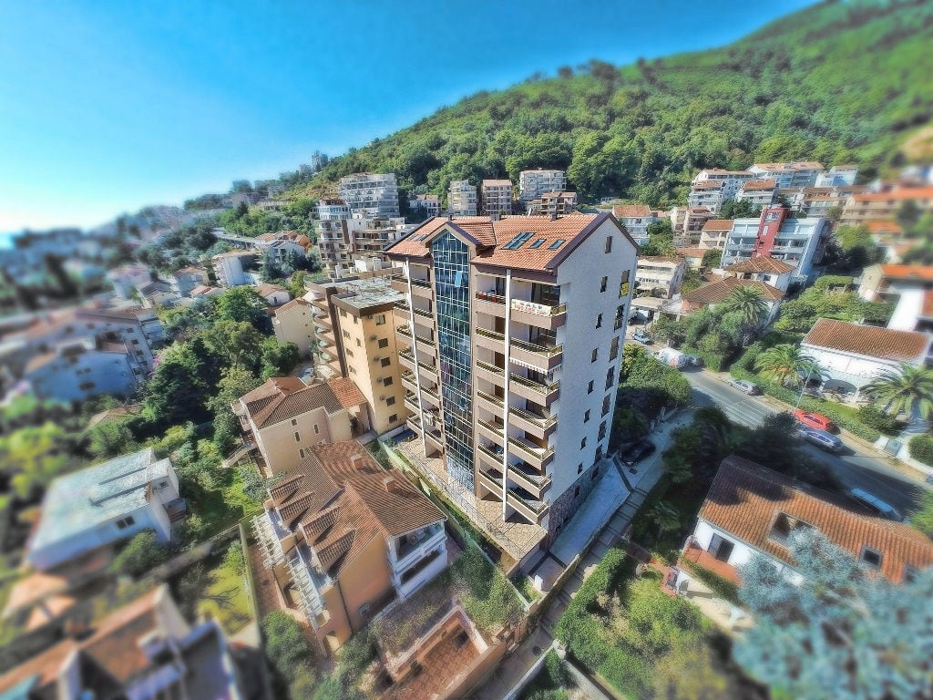 Aerial view of a multi-apartment residential building with balconies in the city of Budva, Montenegro, surrounded by mountains and greenery.