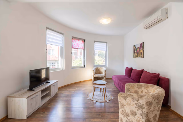 Helles Wohnzimmer mit lila Sofa und TV-Bereich in einer Wohnung in Bečići, Montenegro. Modernes Interieur mit Laminatboden.