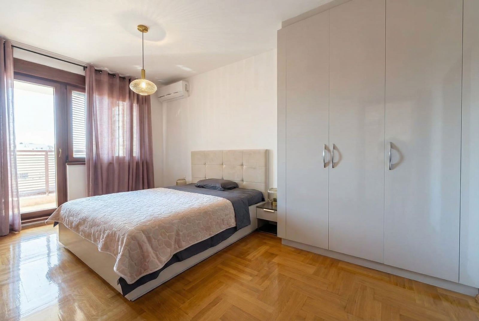 Jasna sypialnia z podwójnym łóżkiem i szafą w mieszkaniu w Rafailovici, Czarnogóra. Parkiet i wyjście na balkon.