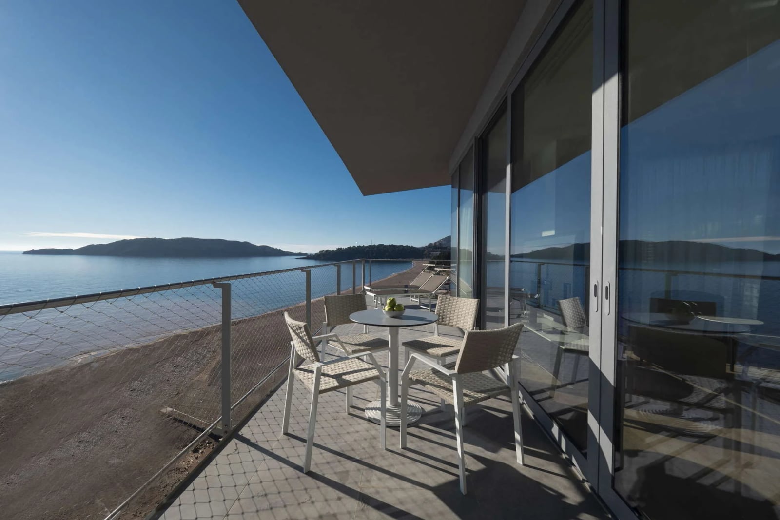 Prostran balkon sa pletenim nameštajem i panoramskim pogledom na more u apartmanima u Bečićima, Crna Gora