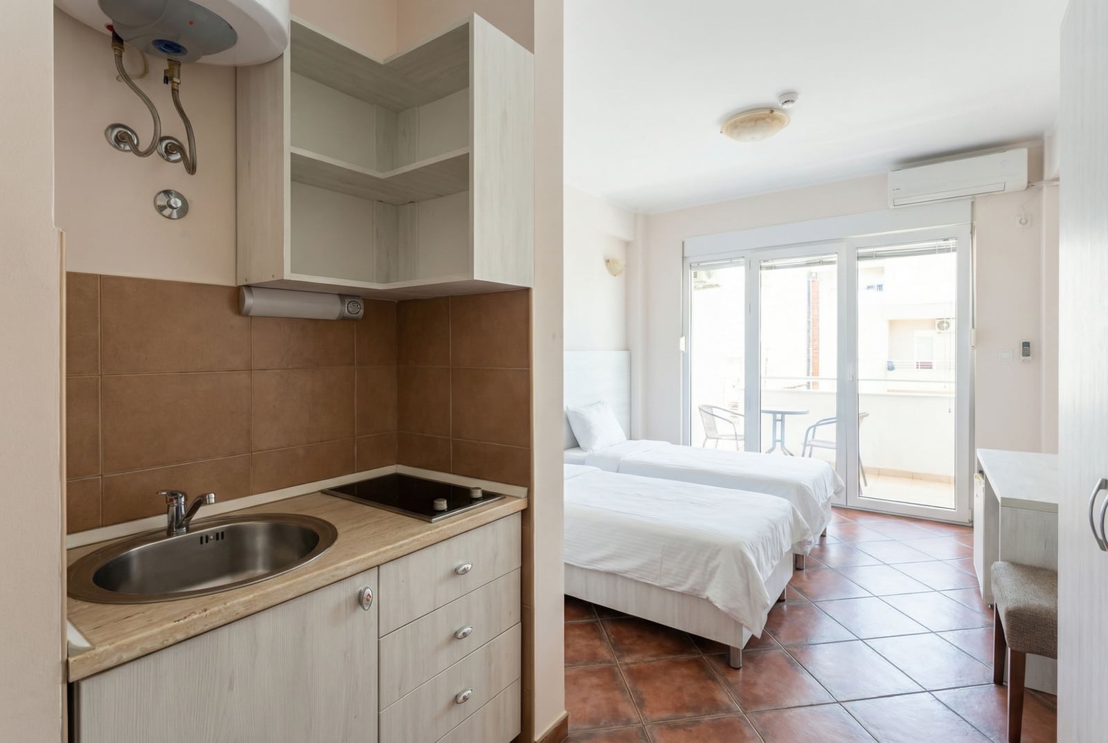 Kuhinja-studio sa dva kreveta i izlazom na balkon u hotelu, Bečići, Crna Gora. Svetao enterijer sa pločicama na podu.
