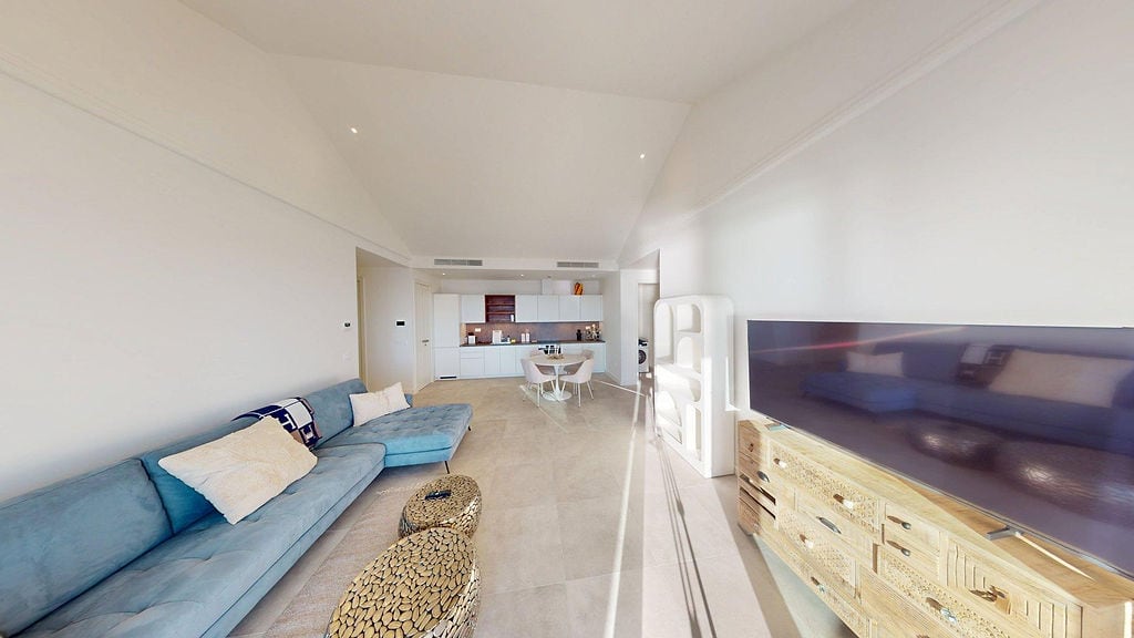 Modernes Wohnzimmer mit blauem Sofa und Küche in der Wohnanlage Lustica Bay, Montenegro. Helle Inneneinrichtung mit TV-Bereich.