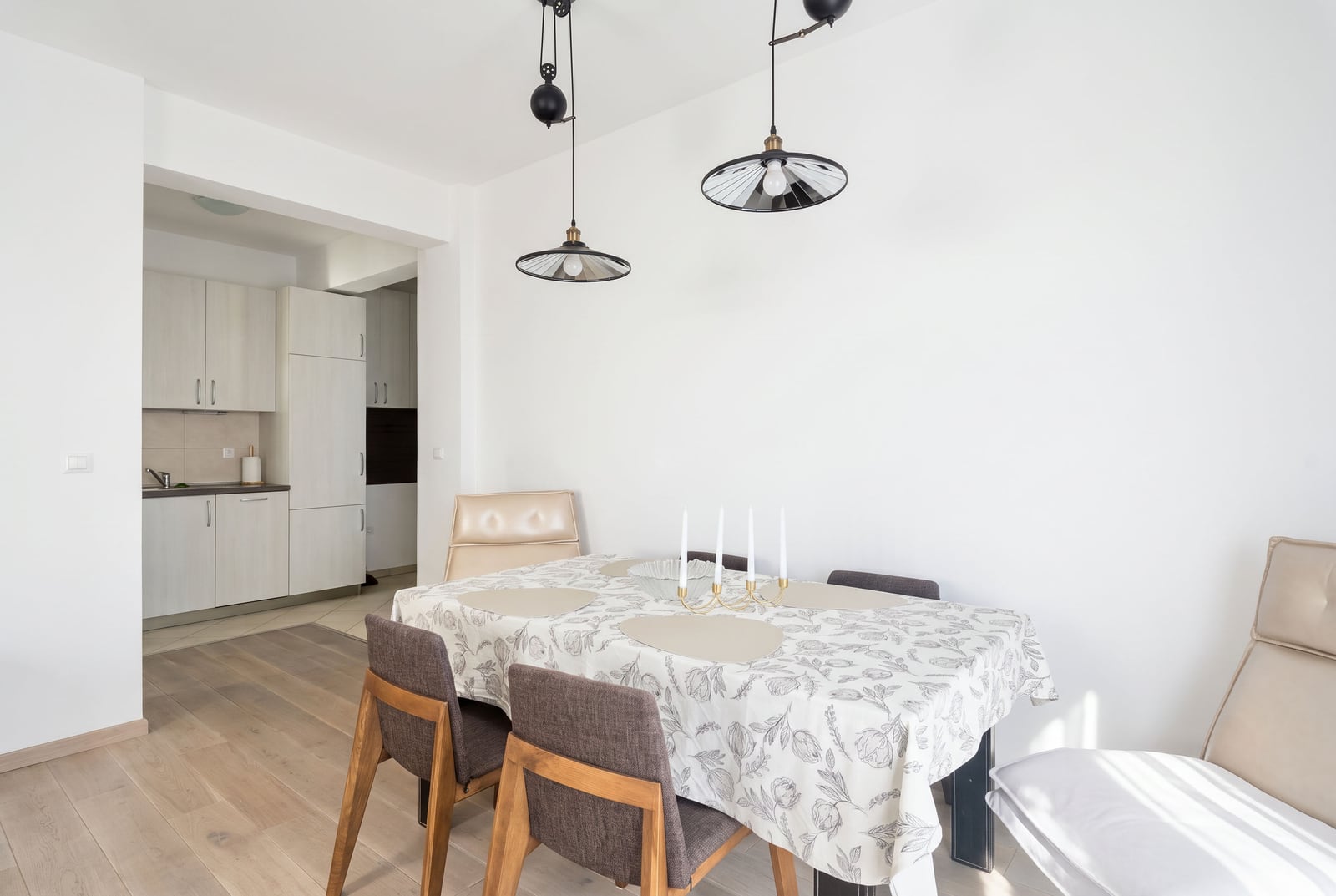 Essbereich in der Wohnung in Budva: Tisch mit grauer Tischdecke, Stühle, moderne Leuchten und helle Küche in Montenegro