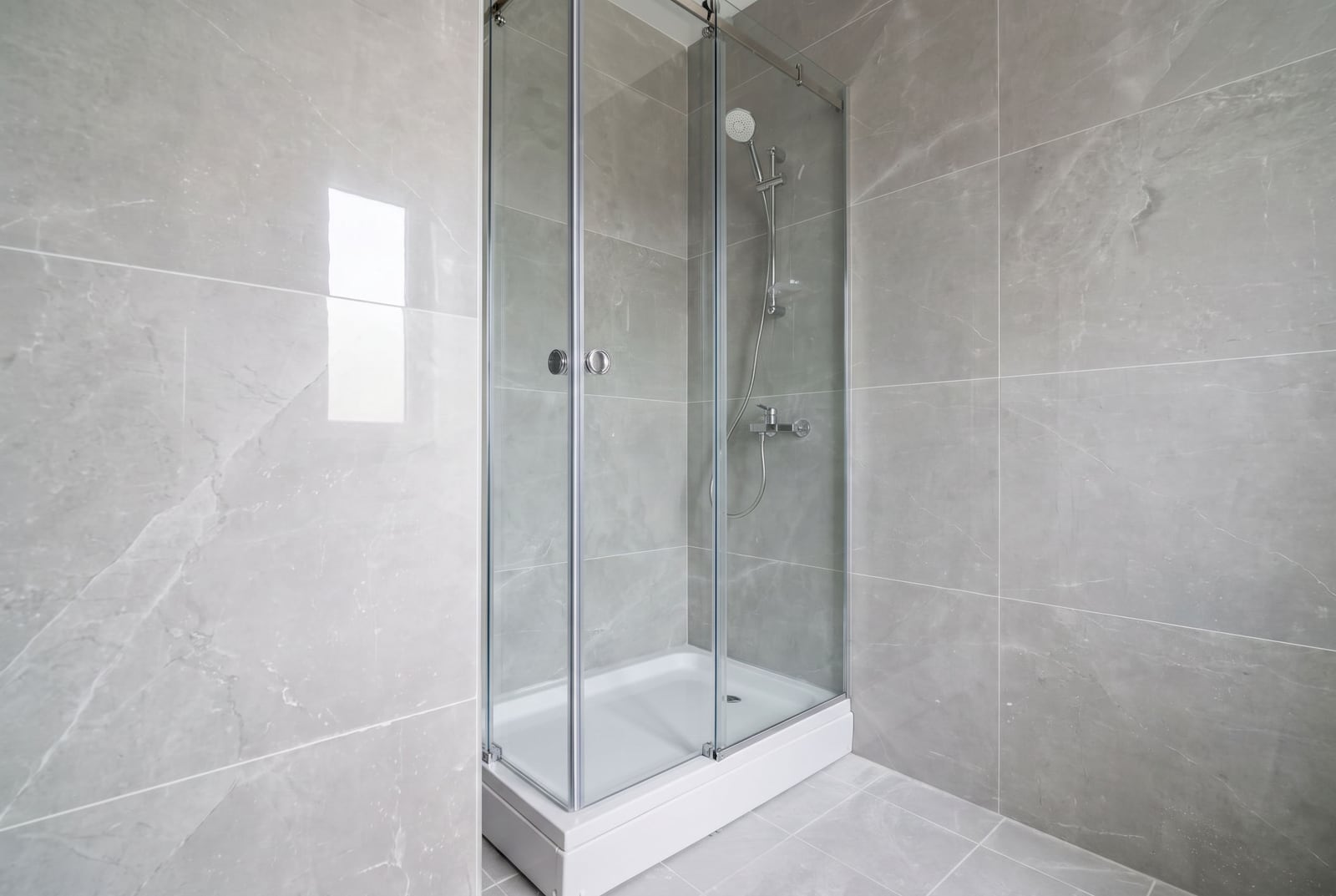 Modern shower cabin in the bathroom of an apartment in the city of Bar, Montenegro, finished with gray marble-look tiles.