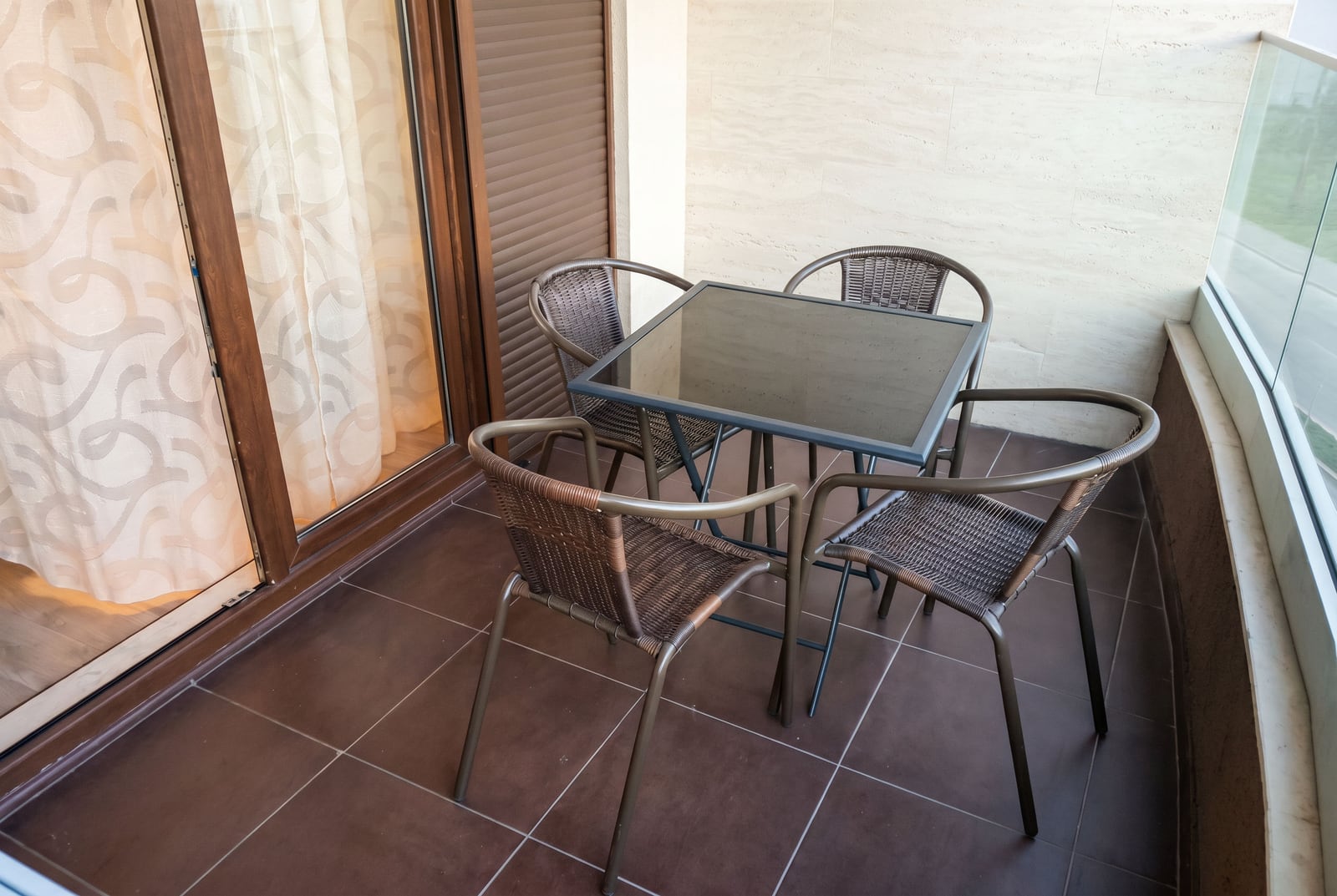 Cozy balcony with wicker furniture in a Budva apartment, Montenegro: a glass-top table and four chairs.
