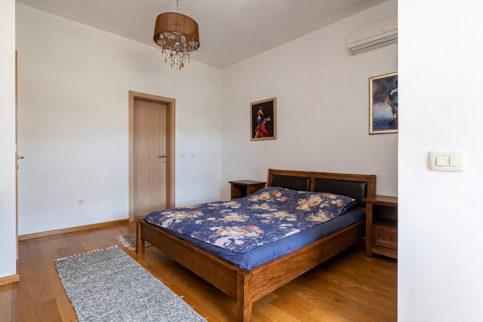 Bedroom with a wooden bed, nightstands, and parquet flooring in an apartment in Bečići, Montenegro.