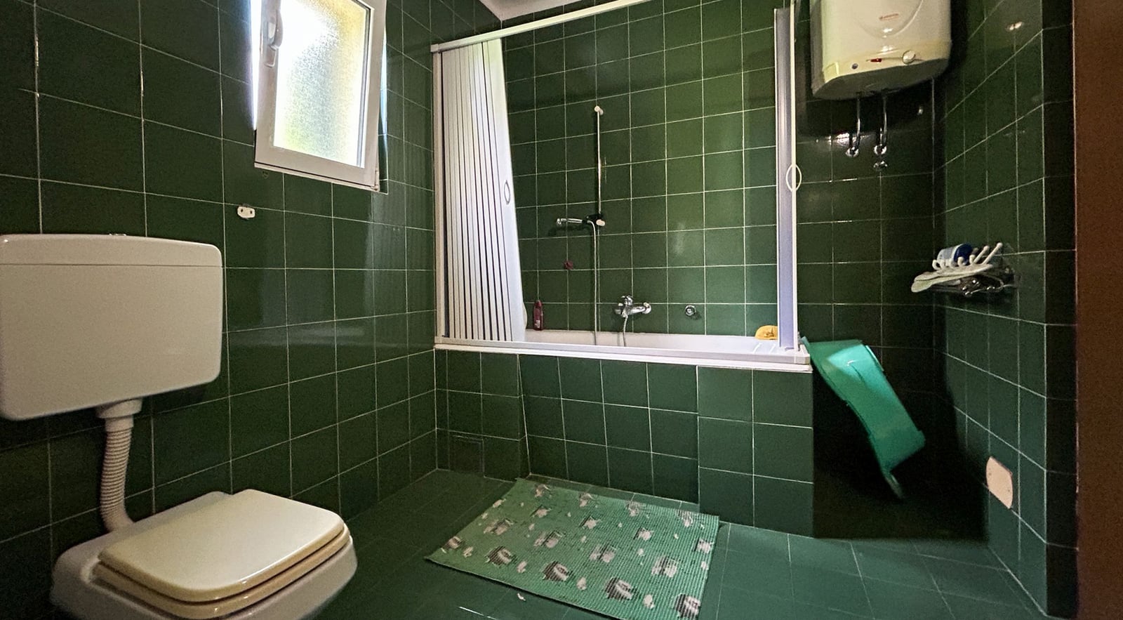 Badezimmer mit grünen Fliesen, Badewanne und Boiler in einer Villa in Dobrota, Montenegro. Innenraum des Badezimmers im Haus.