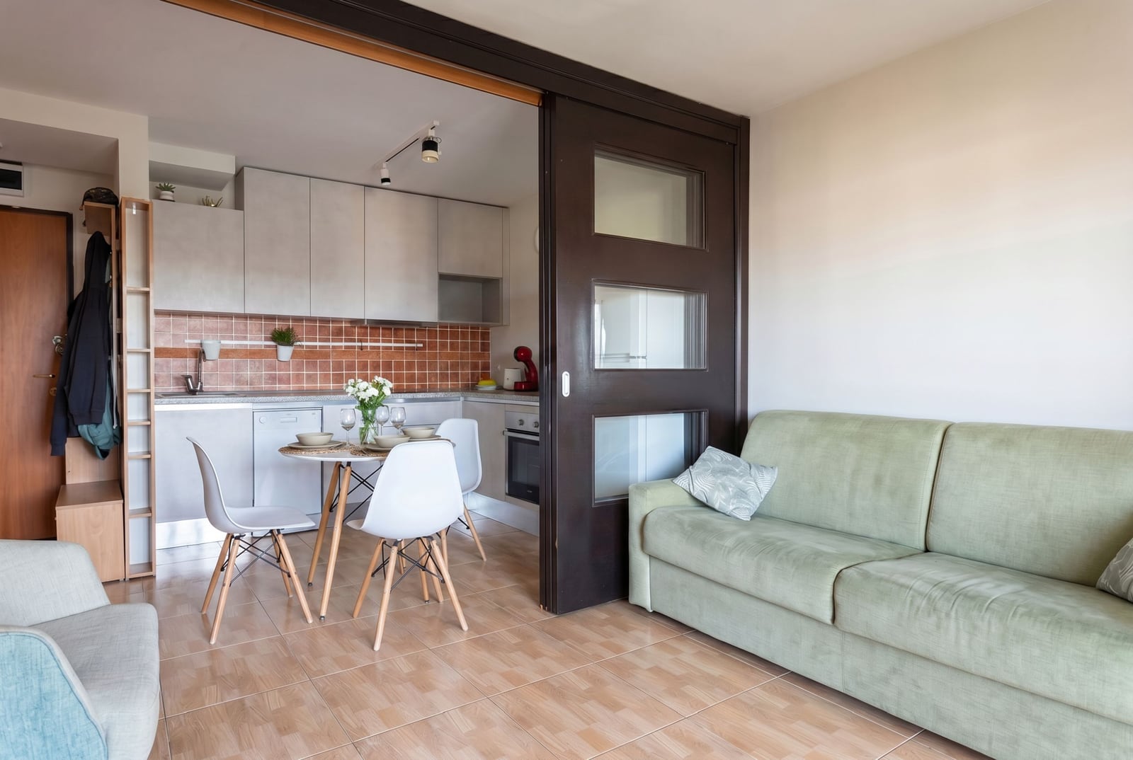 Living room with kitchen in an apartment in Budva, Montenegro: light-colored sofa, dining area, and sliding partition.