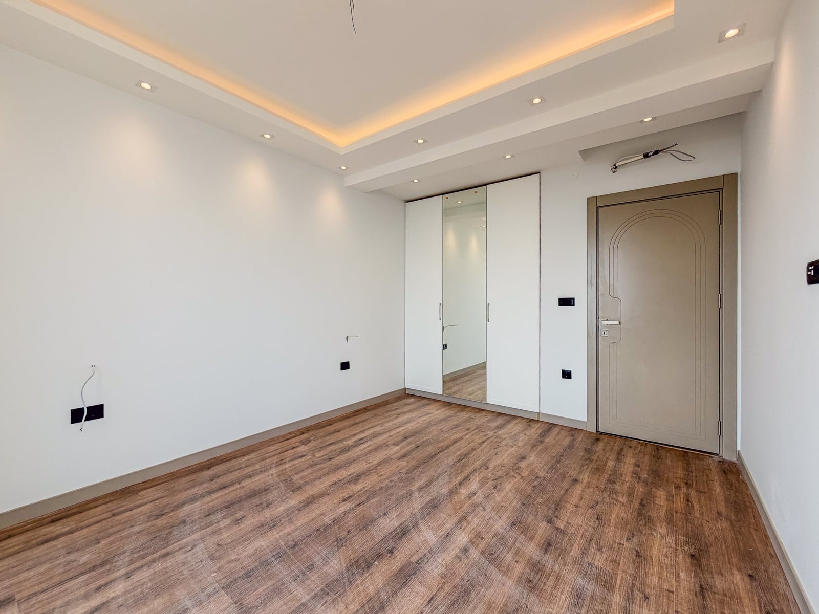 Bright bedroom with laminate flooring, white walls, a built-in wardrobe with a mirror, and an interior door in an apartment in Budva, Montenegro