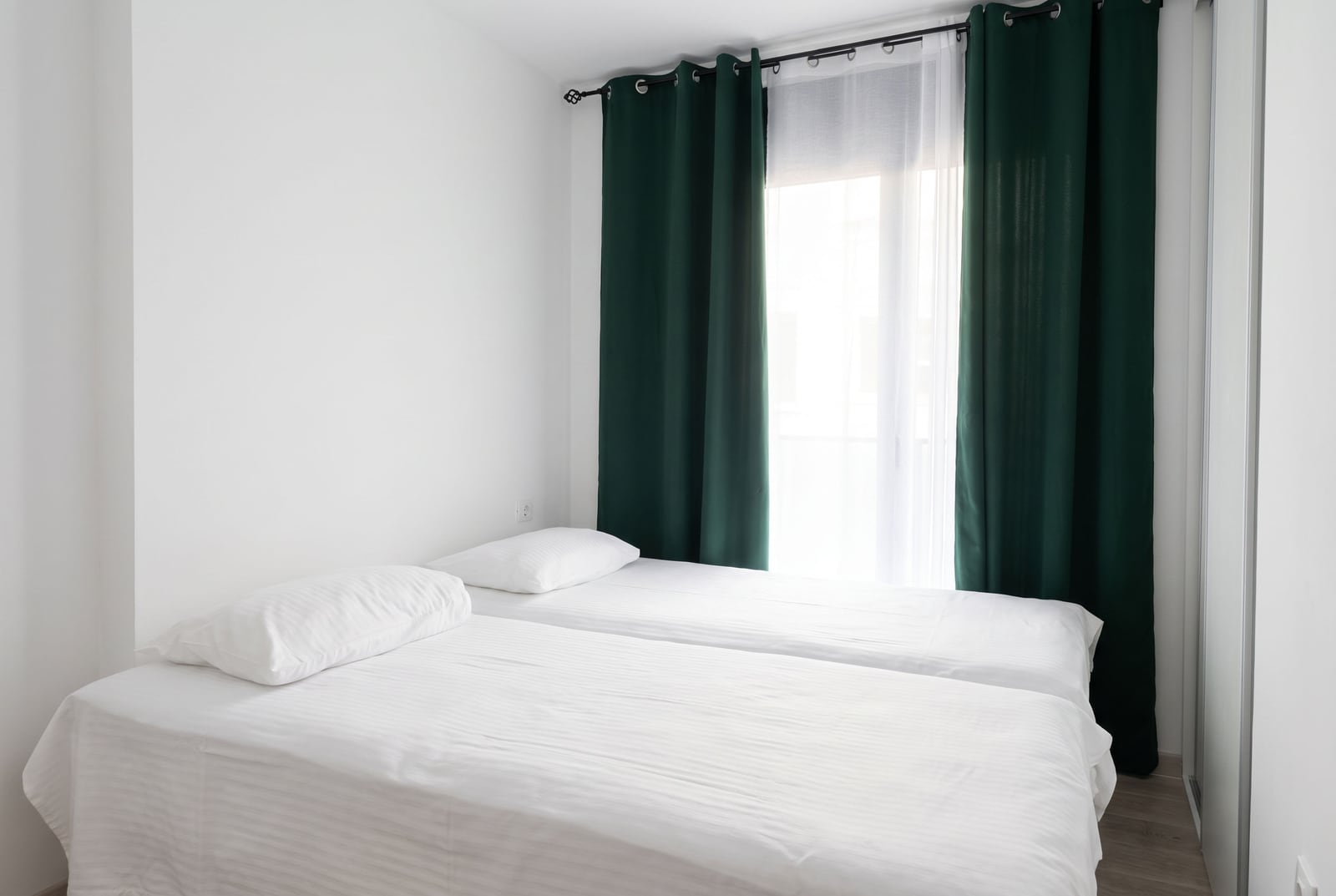 Helle Schlafzimmer mit zwei Betten und grünen Vorhängen in einer Wohnung in Budva, Montenegro