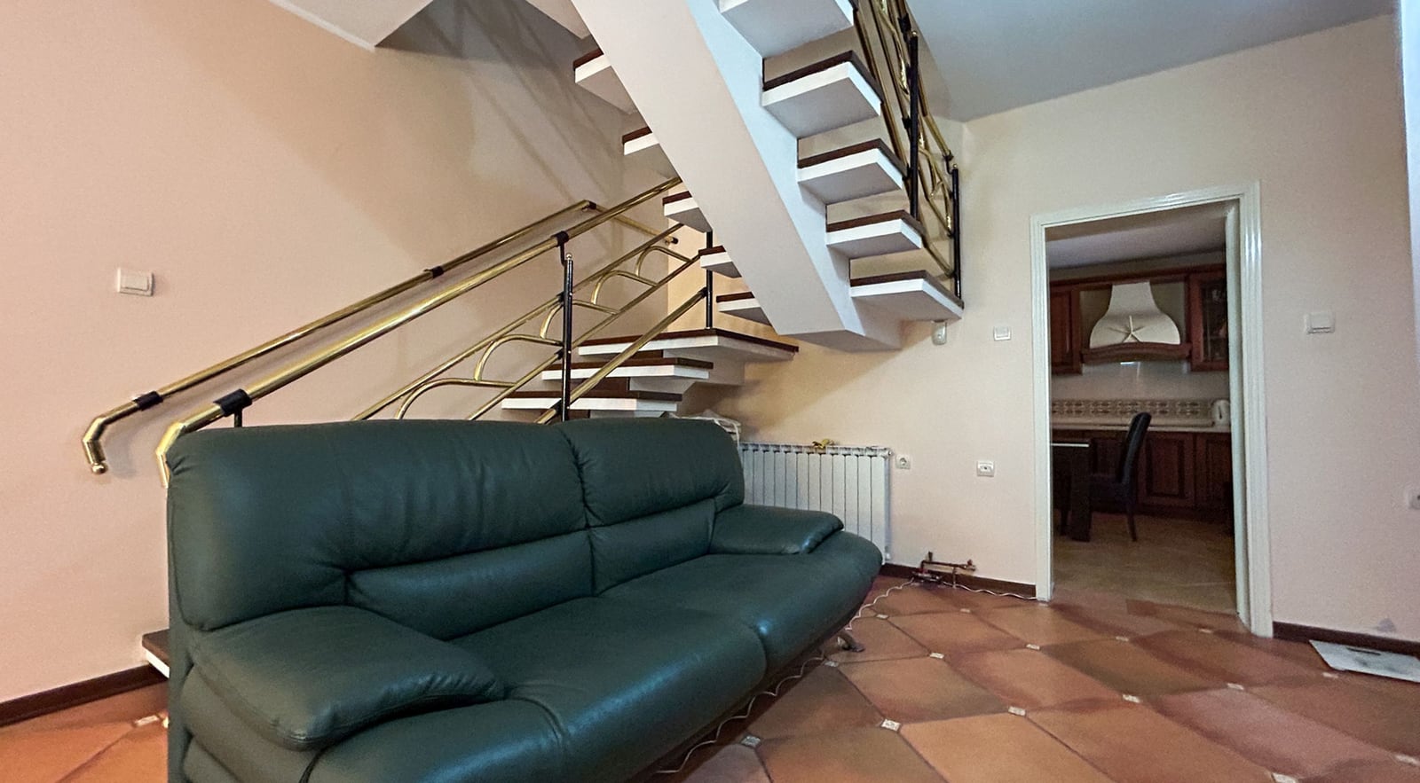 Wohnzimmer mit Ledersofa und Treppe in einer Villa in Dobrota, Montenegro: Innenraum mit Fliesen und Zugang zur Küche.
