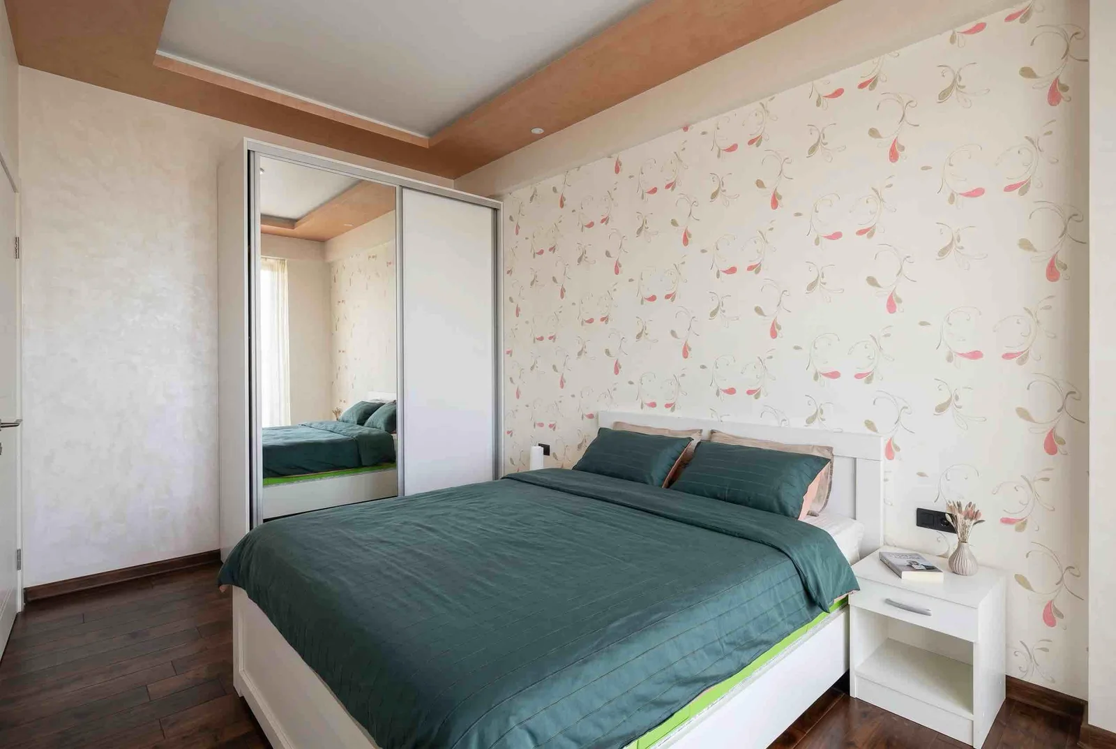 Bedroom featuring a double bed with green bedding, a white mirrored wardrobe, floral wallpaper, and dark wood flooring.
