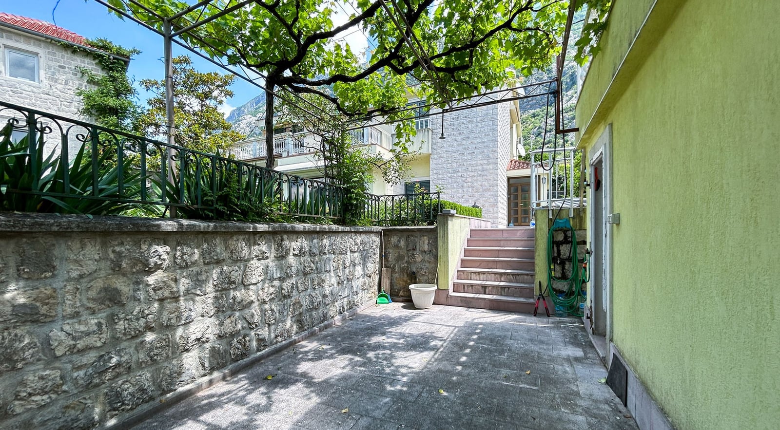 Gemütlicher Innenhof mit Steinmauer und Weinpergola an der Villa in Dobrota, Montenegro.
