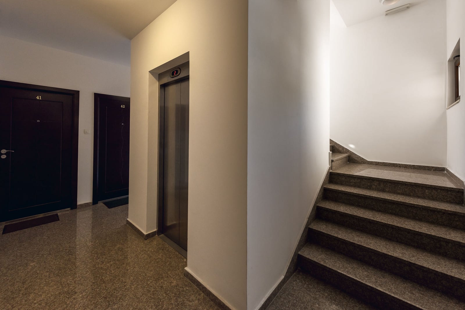Modern entrance with an elevator and staircase in a residential building, Budva, Montenegro: bright interior, stone finish.