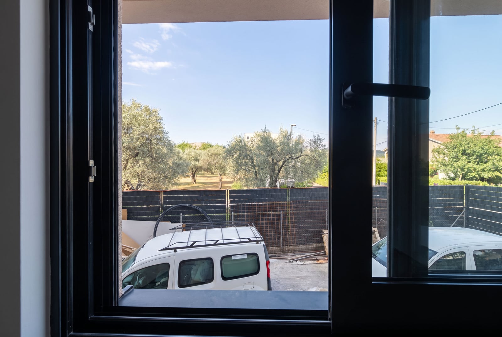 View from the apartment window in the city of Bar, Montenegro: parking, olive trees, and modern double-glazed windows in the interior.