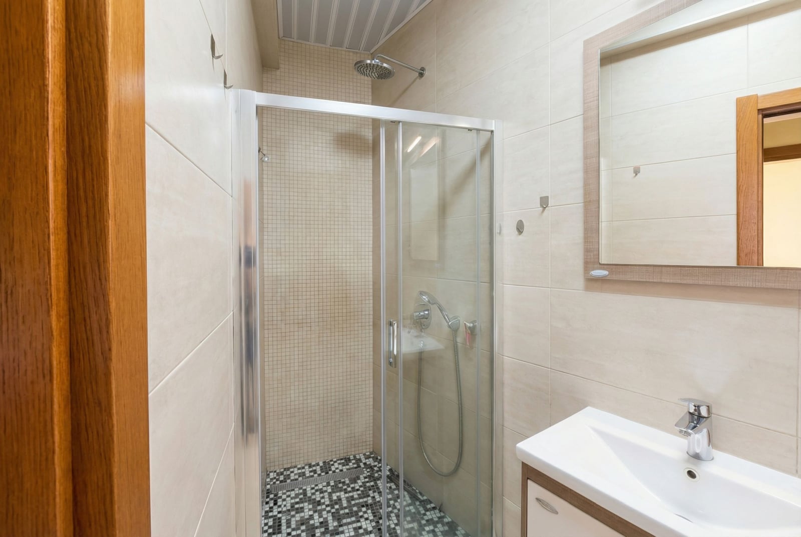 Modern bathroom in an apartment in Petrovac, Montenegro: shower cabin, light-colored tiles, and a mirror above the sink.