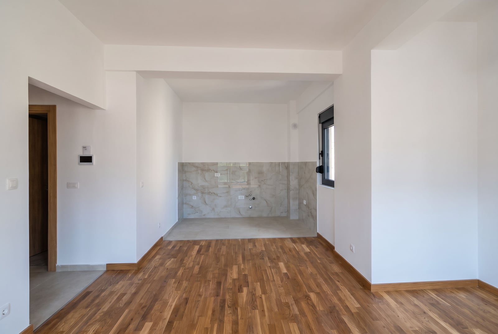 Bright kitchen in a new apartment in the city of Bar, Montenegro: parquet flooring, marble backsplash, and prepared utilities.