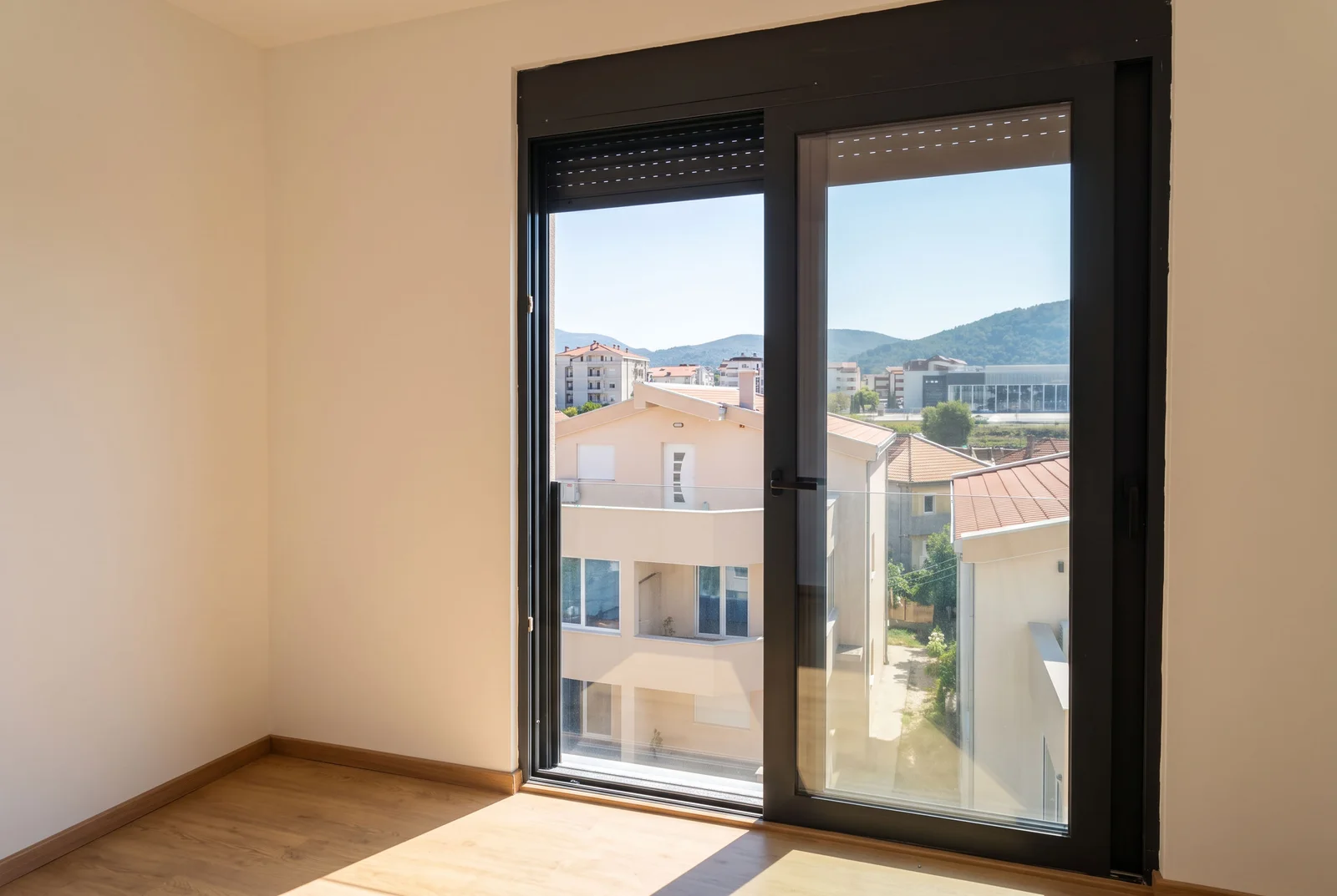 Puste pomieszczenie z drewnianą podłogą i dużą czarną szklaną drzwiami na balkon.