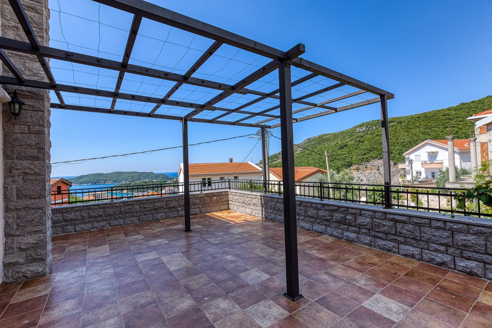 Terrasse spacieuse avec pergola et vue sur la mer dans une villa, Bečići, Monténégro. Finitions en pierre et sol carrelé.