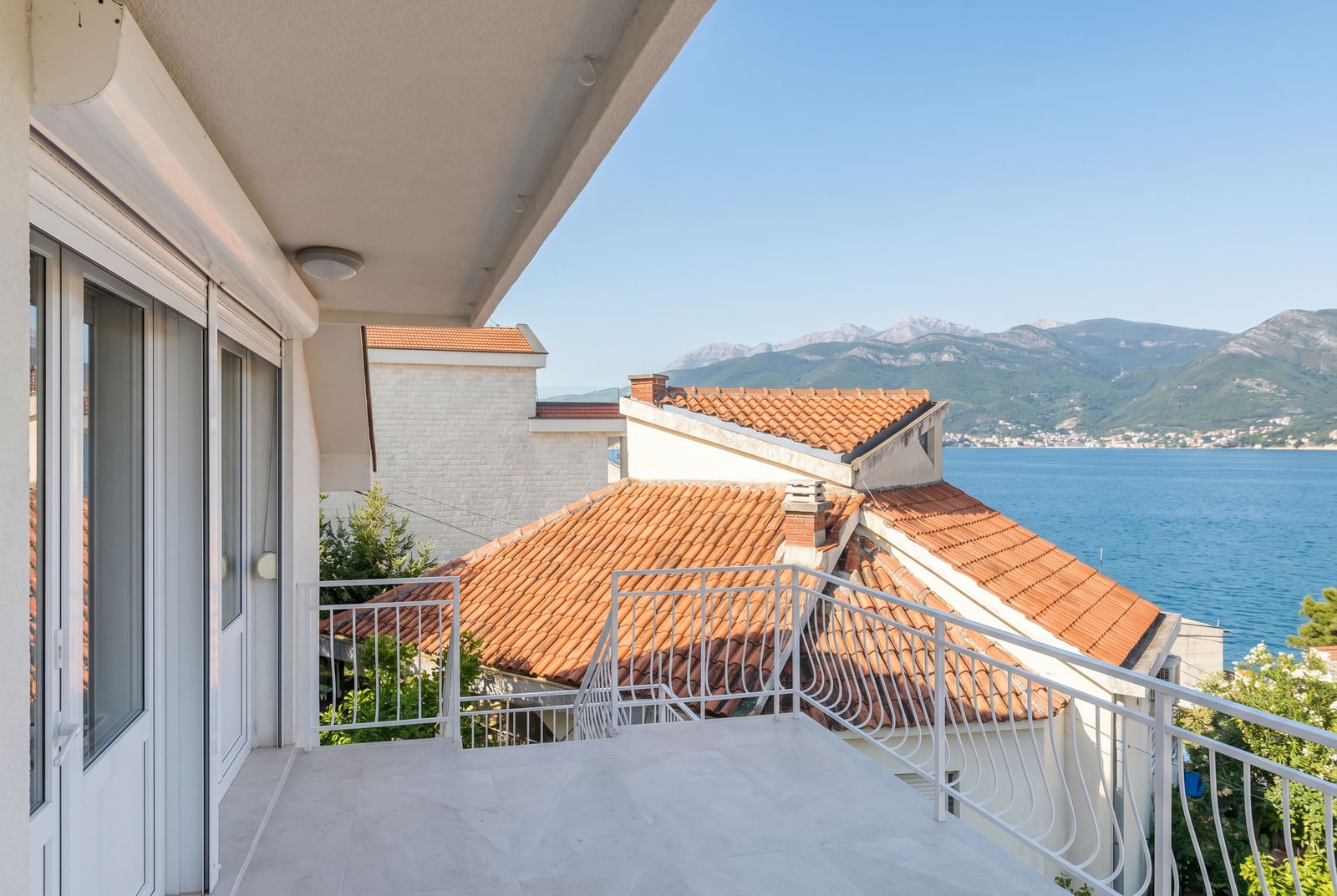 Balcon spacieux avec vue sur la mer et les montagnes dans une maison à Krašići, Monténégro : finitions lumineuses et garde-corps en fer forgé.