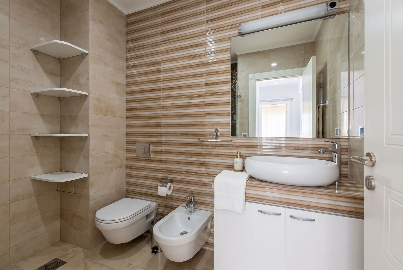 Modern bathroom with white sanitary ware, bidet, and beige-toned tiles in an apartment, Budva, Montenegro.