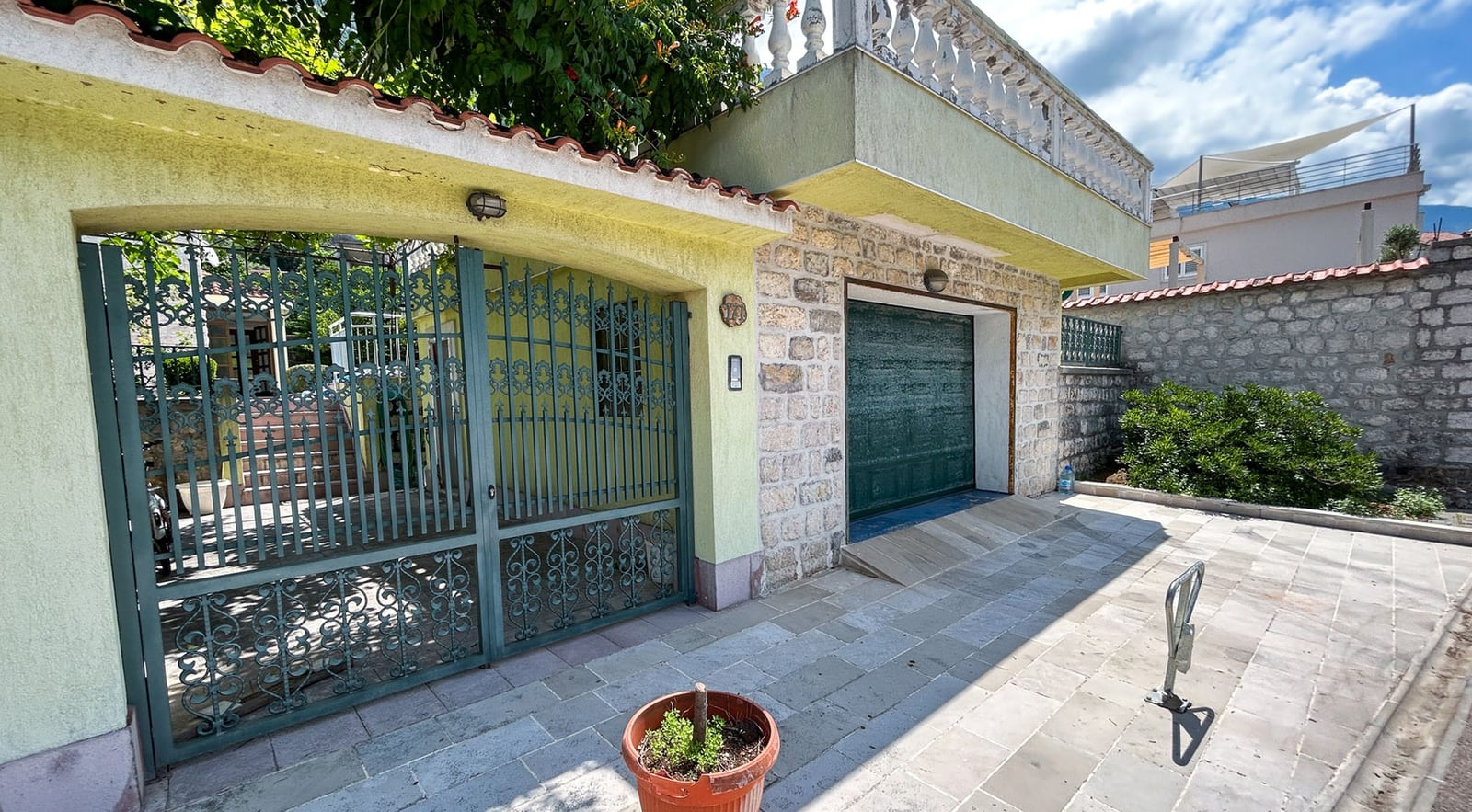 Fassade der Villa in Dobrota, Montenegro: Steinverkleidung, Garagentor und schmiedeeisernes Tor mit Terrasse im zweiten Stock.