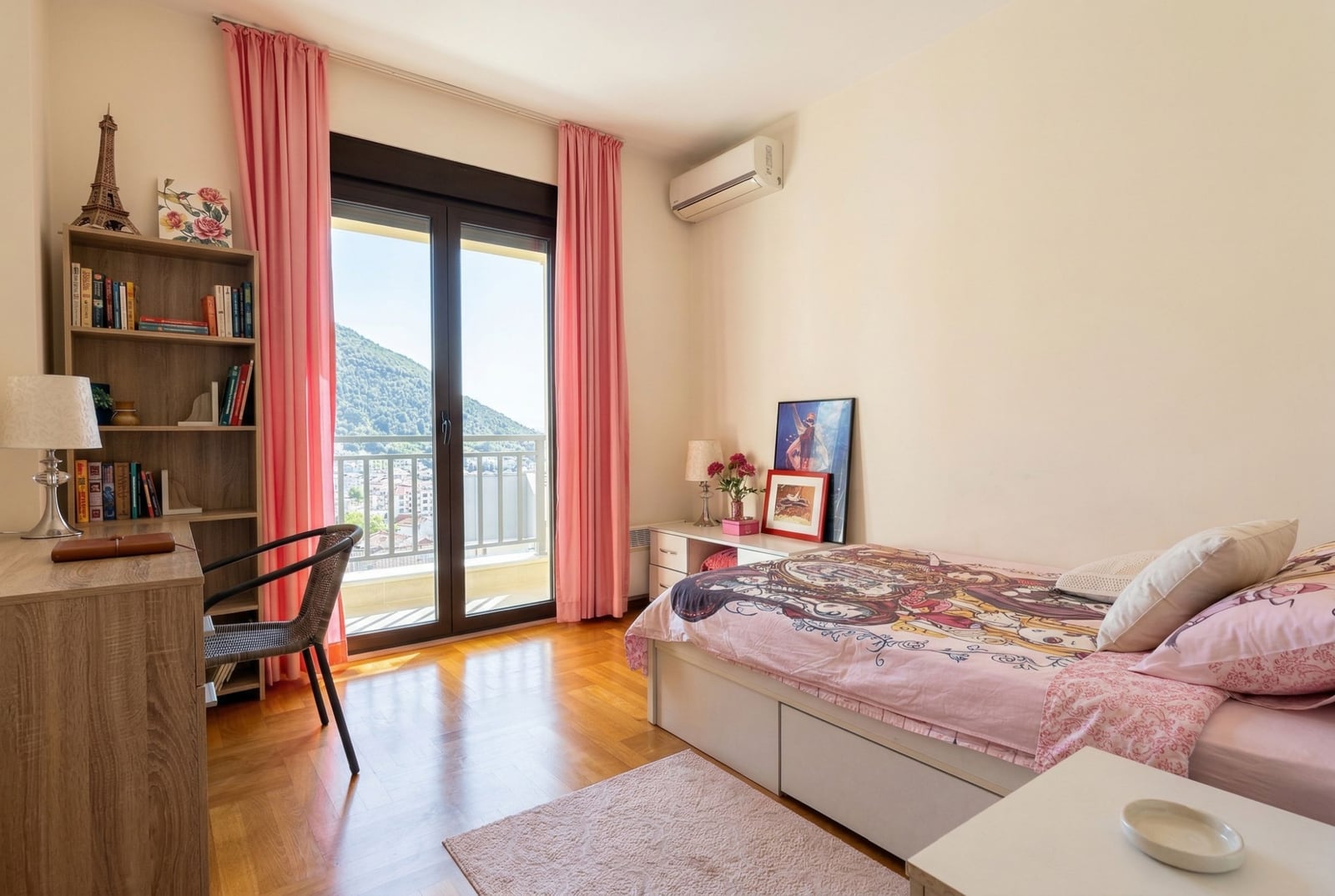 Spavaća soba u stanu u Budvi, Crna Gora: krevet, radni sto, polica, parket i izlaz na balkon s pogledom na planine.