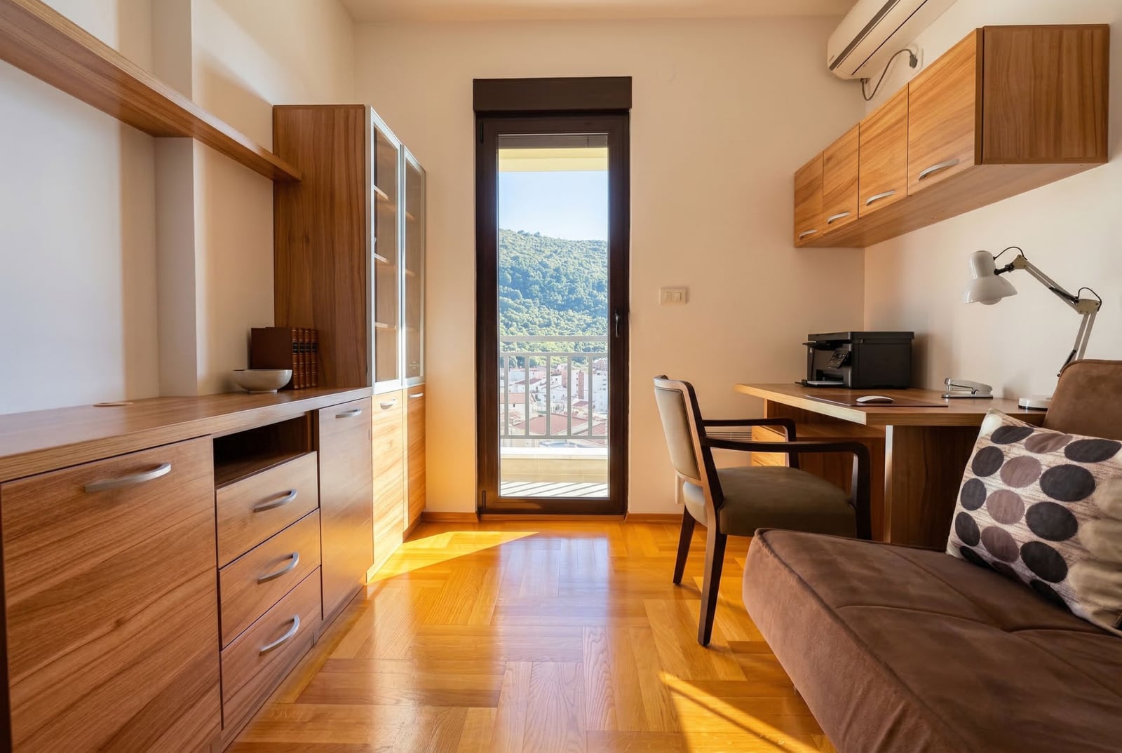 Radna soba u stanu u Budvi, Crna Gora: drveni nameštaj, parket, balkon s pogledom na planine i grad.