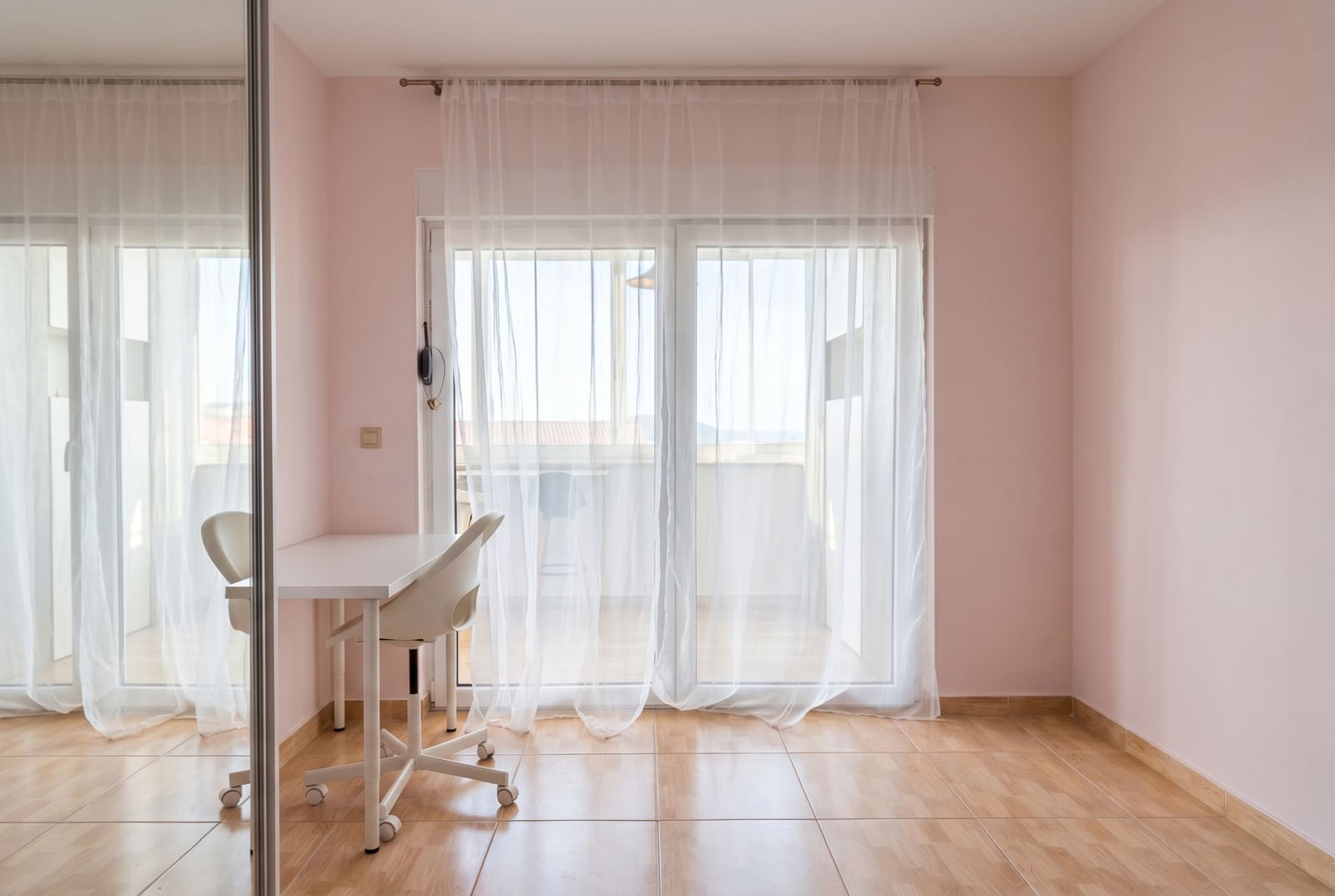 Bright bedroom in an apartment in Budva, Montenegro: desk, mirrored wardrobe, balcony access, and tiled floor.