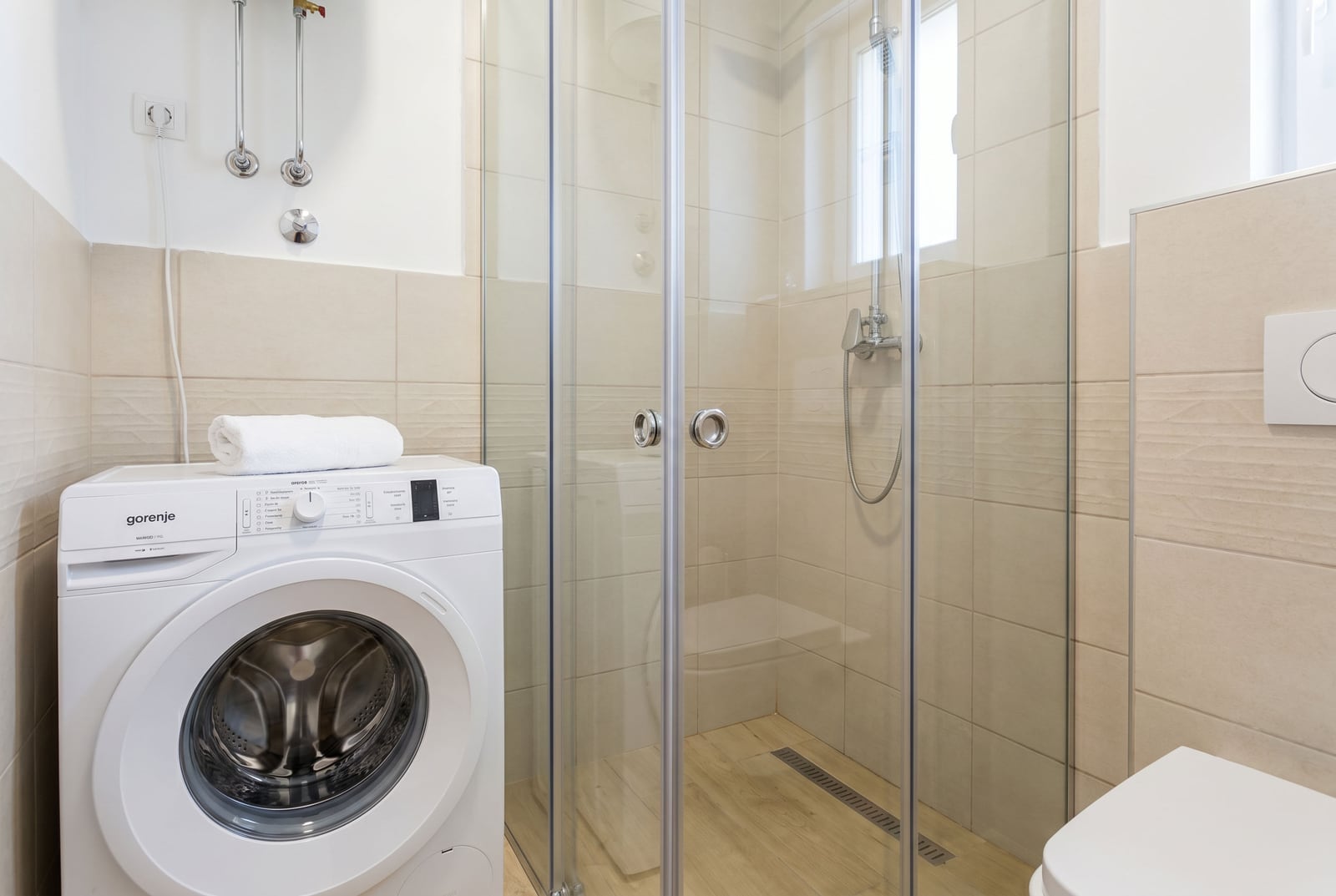 Moderno kupatilo u stanu u Budvi, Crna Gora: tuš kabina, Gorenje veš mašina i svetle pločice.