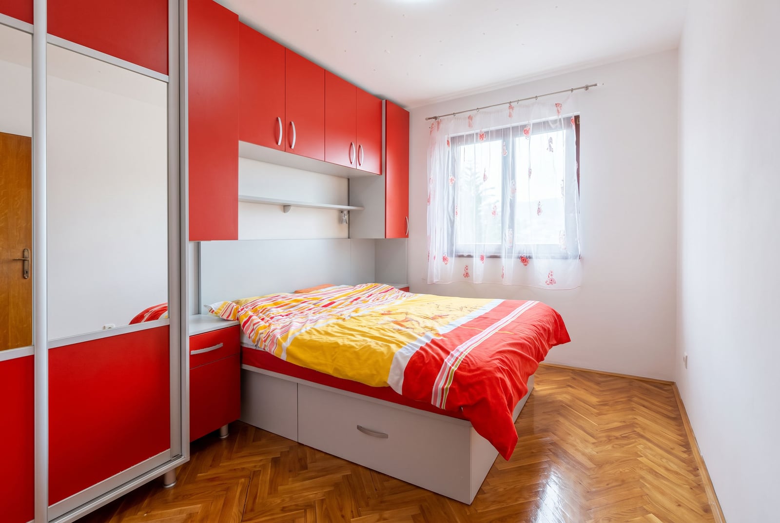 Spavaća soba sa jarkim crvenim nameštajem, ormanom sa ogledalom i parketom u stanu u Budvi, Crna Gora
