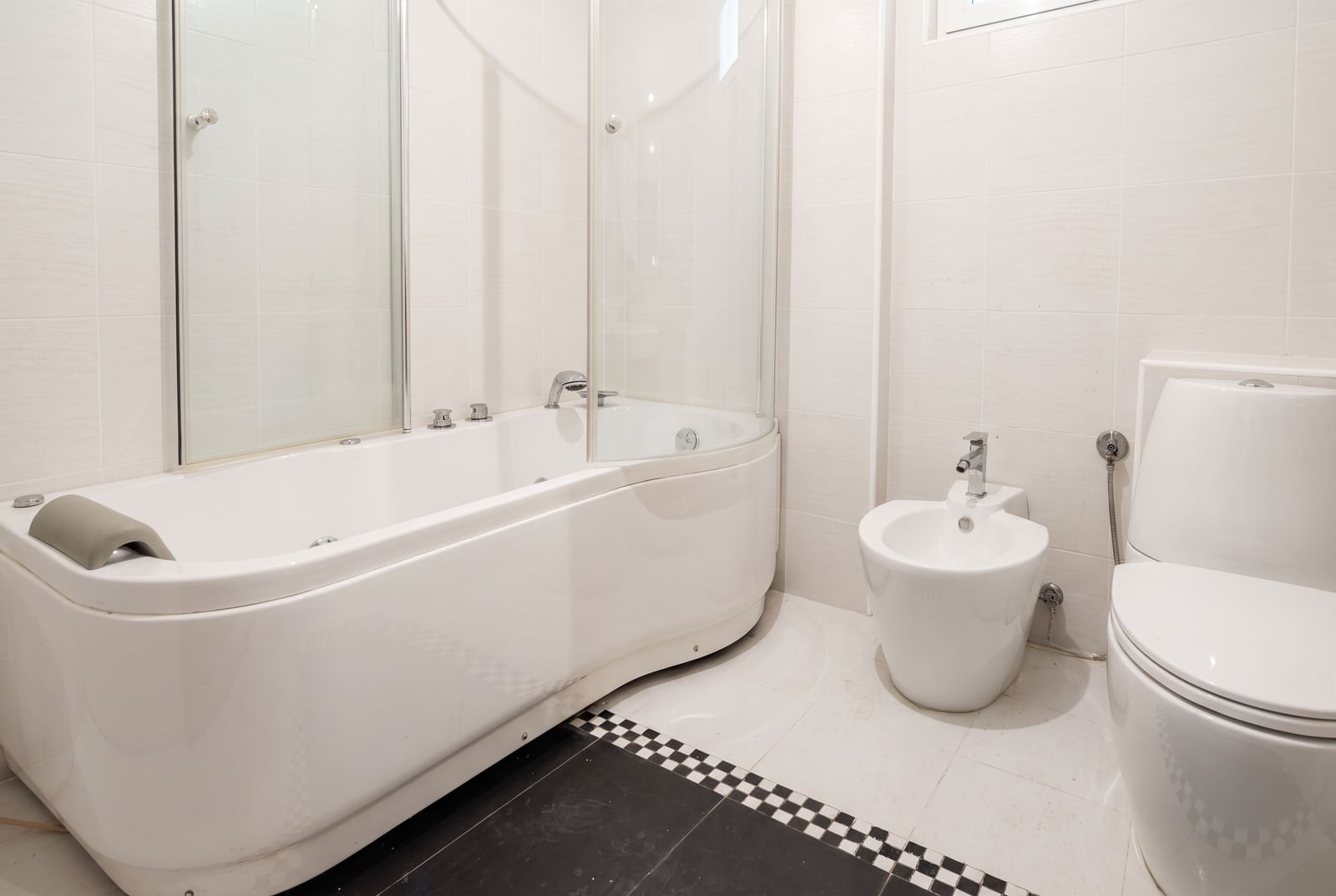 Modern bathroom with a corner bathtub, glass partition, bidet, and light tiles in an apartment in Petrovac, Montene...