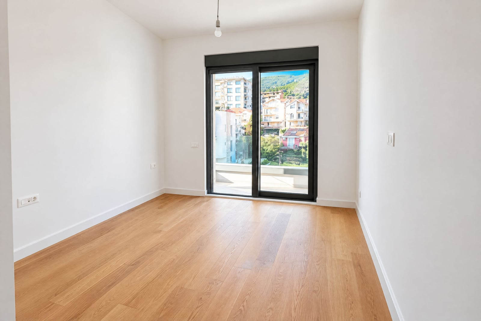 Bright empty bedroom with parquet flooring and a panoramic window with mountain views in an apartment in Becici, Montenegro
