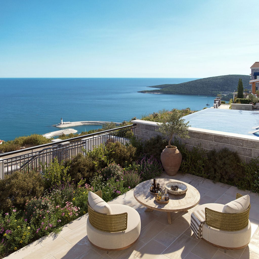 Terrasse mit Pool und Meerblick in der Wohnanlage Luštica, Montenegro: Korbmöbel, Steinverkleidung und Panoramalandschaft.