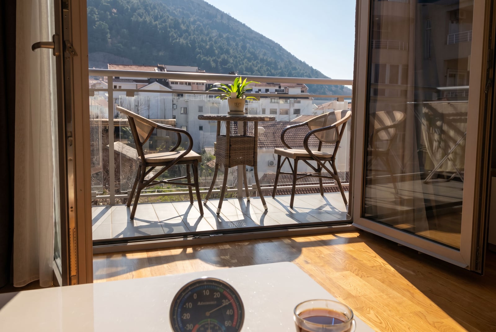 Balkon sa pletenim nameštajem i pogledom na planine u stanu u Budvi, Crna Gora: udobna terasa sa panoramskim zastakljivanjem.