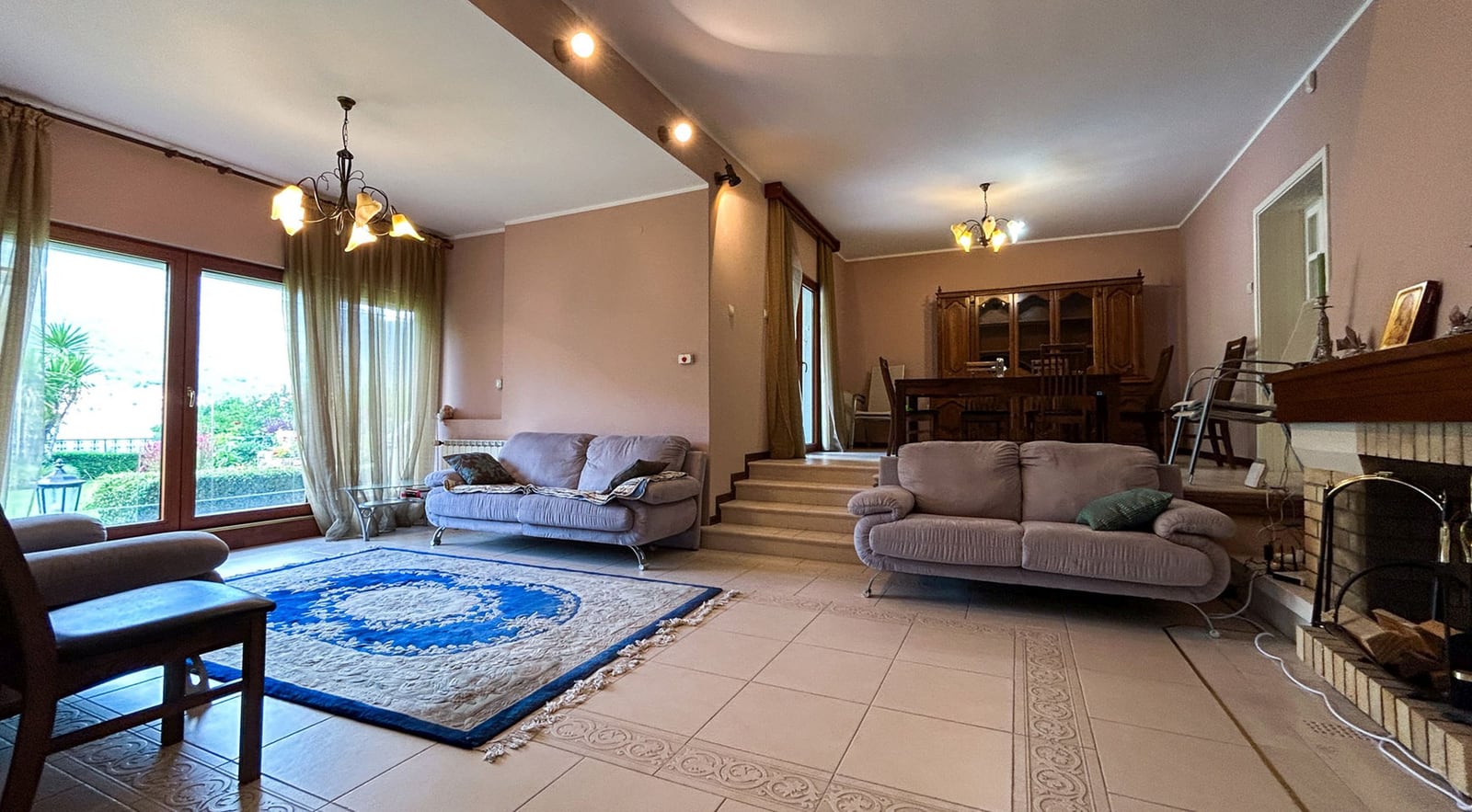 Geräumiges Wohnzimmer mit Kamin und Polstermöbeln in einer Villa in Dobrota, Montenegro: Blick auf den Essbereich und die Terrasse.