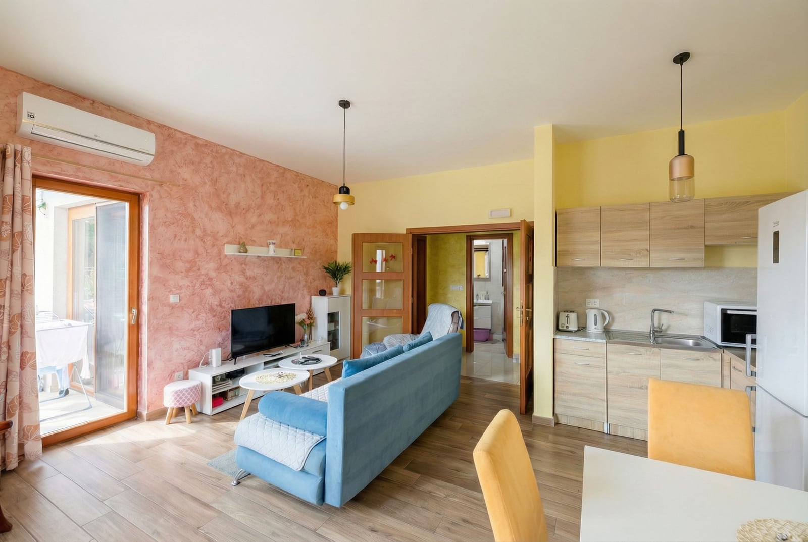Living room with kitchen in an apartment in Petrovac, Montenegro: blue sofa, light furniture, and access to the terrace.
