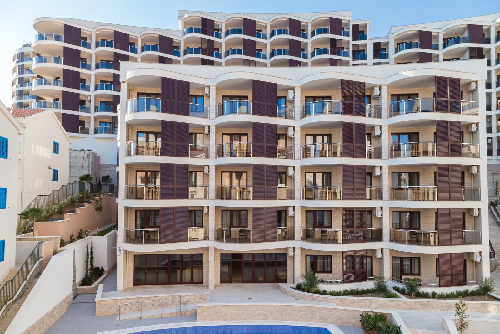 Moderner Wohnkomplex mit Balkonen und Pool in Bečići, Montenegro: Blick auf die mit Stein verkleidete Fassade des Gebäudes.
