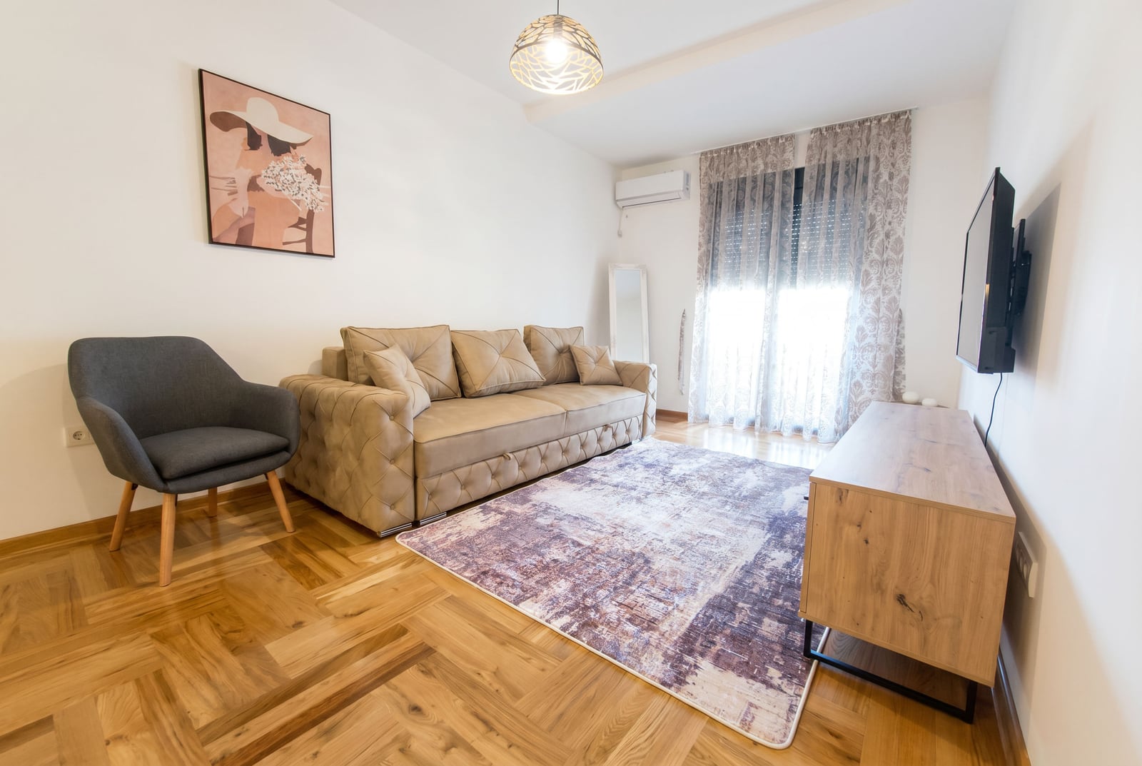 Przytulny salon z beżową sofą, fotelem i parkietem w apartamencie w Rafailovici, Czarnogóra. Nowoczesne wnętrze.