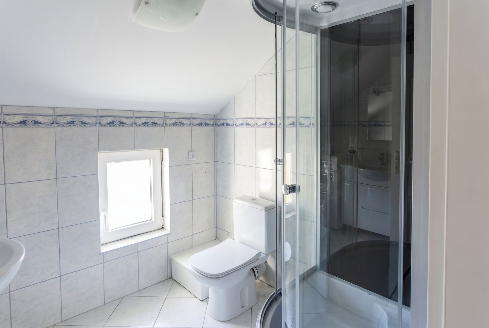Salle de bain lumineuse dans une maison à Krašići, Monténégro : cabine de douche, sanitaires et fenêtre sous les combles.