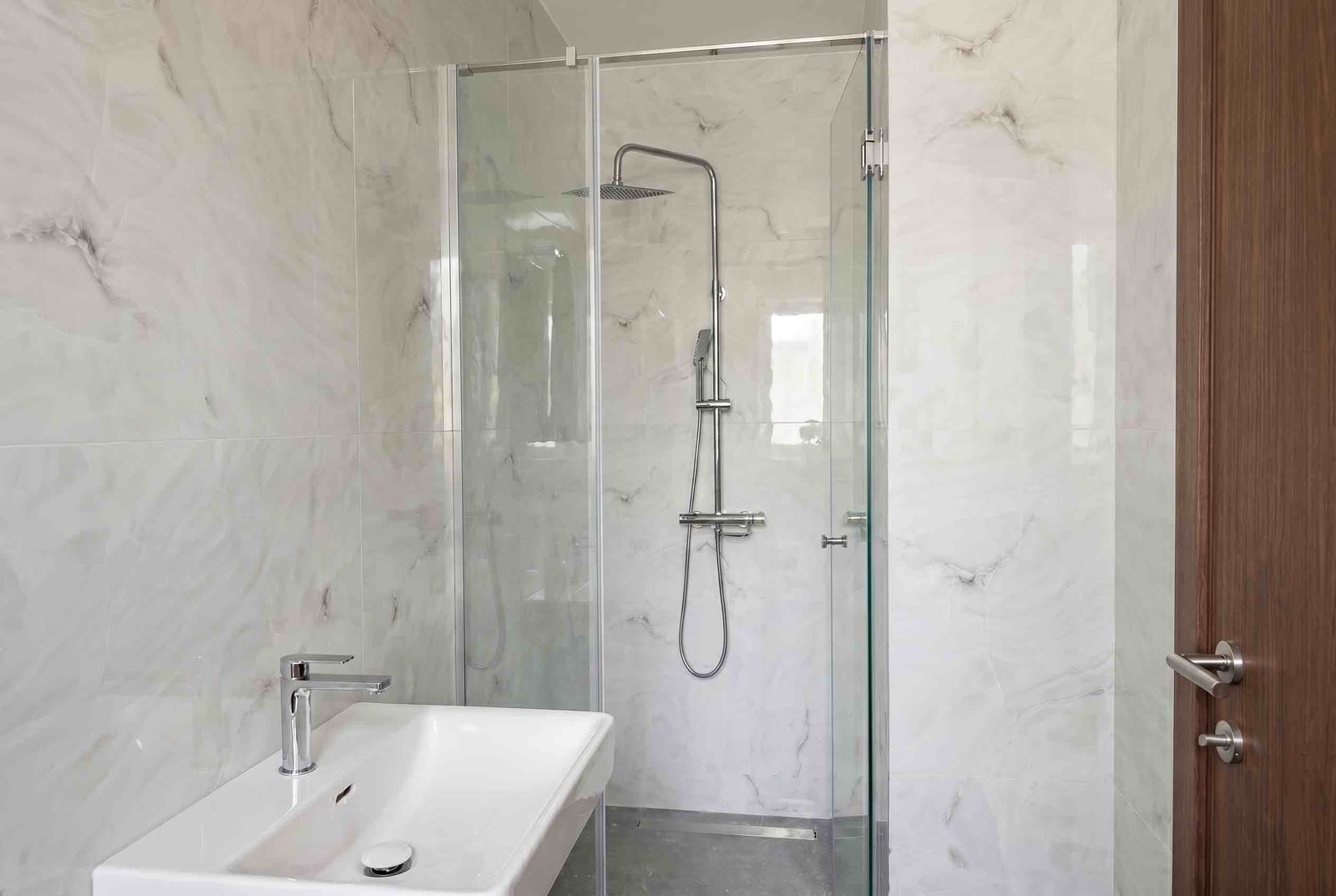 Modern bathroom in an apartment in Budva, Montenegro: shower cabin, light marble-look tiles, and plumbing fixtures.