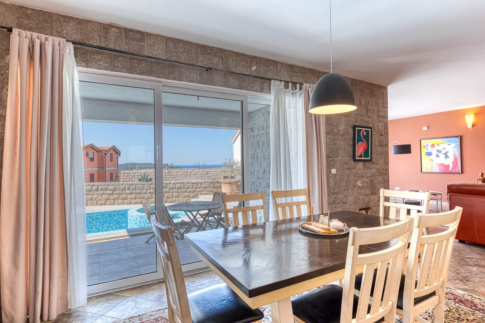 Salon avec coin repas dans une villa à Bečići, Monténégro : vue sur la terrasse avec piscine et la mer à travers des baies vitrées panoramiques.