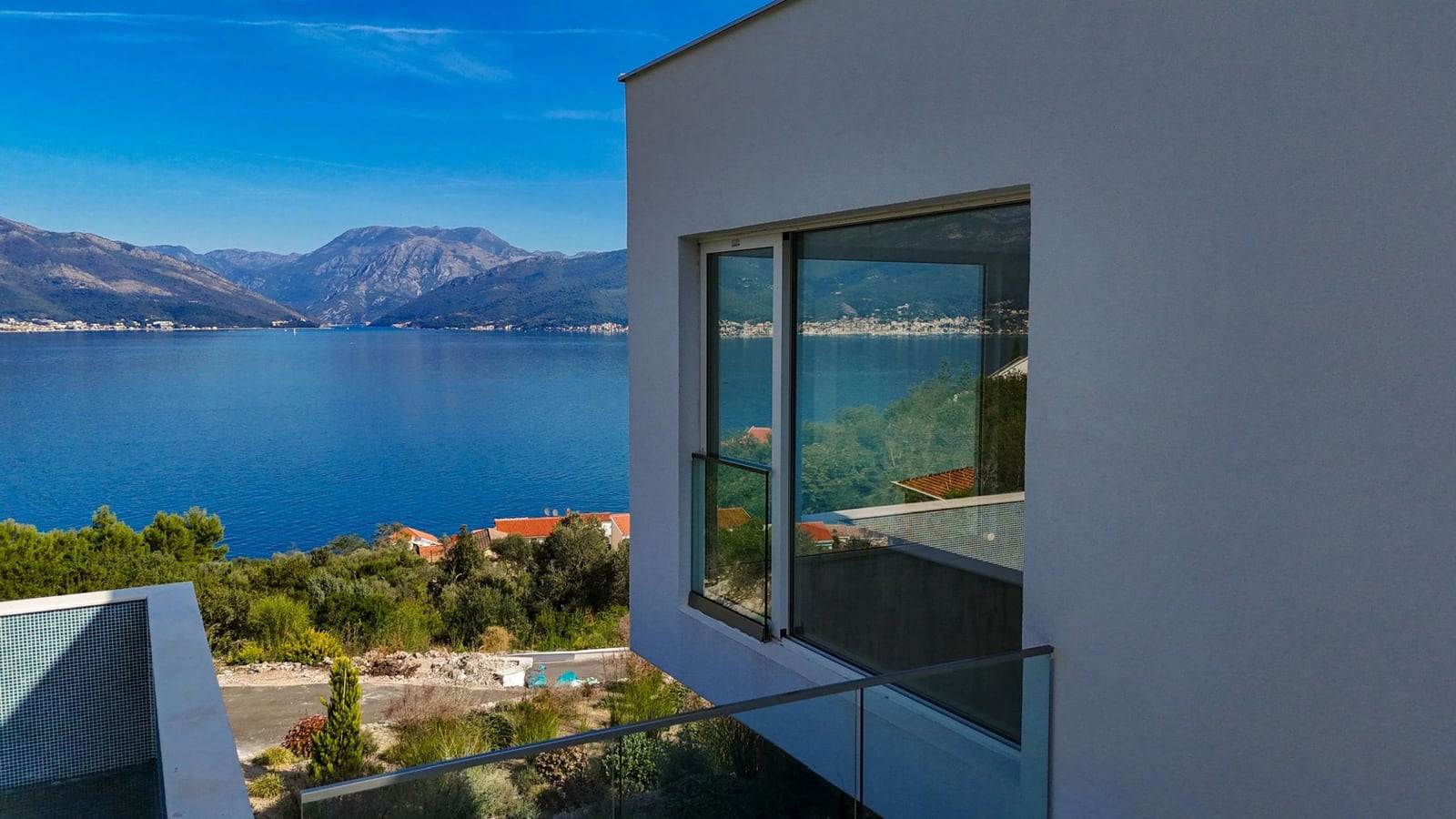 Moderne Villa in Krašići, Montenegro mit Panoramablick auf das Meer, die Berge und einem Glasbalkon vor der Kulisse der Bucht.