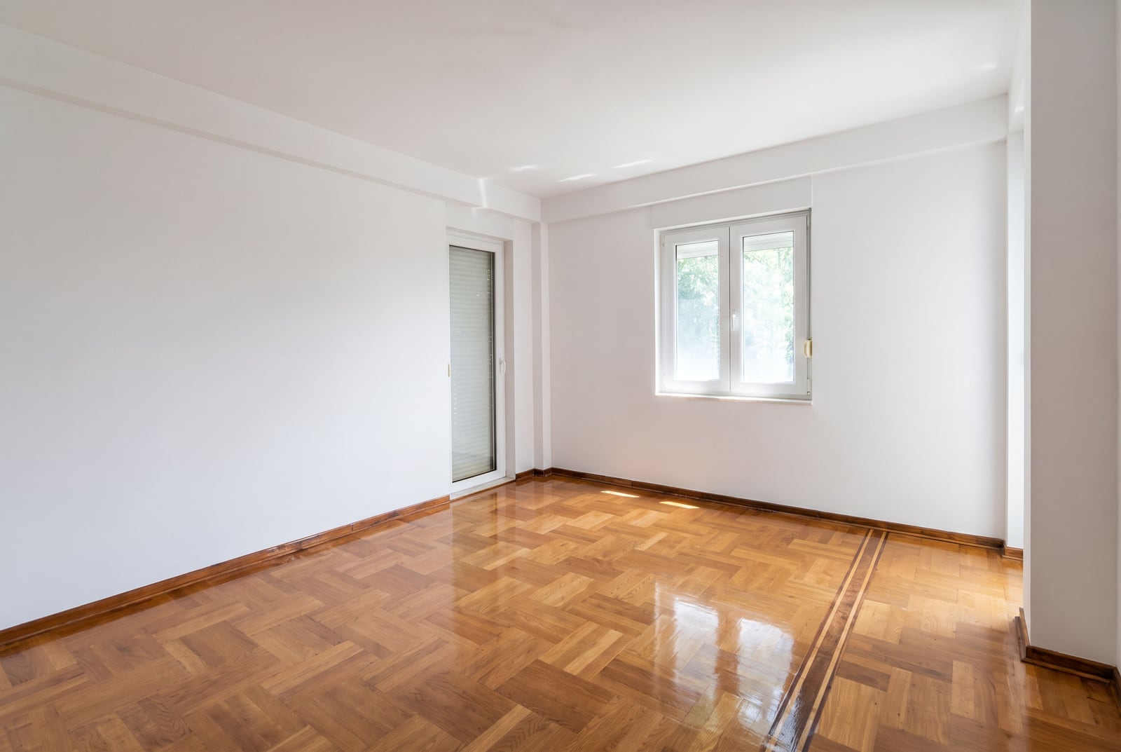 Bright empty living room with white walls, parquet flooring, and access to a balcony in an apartment in Petrovac, Montenegro.