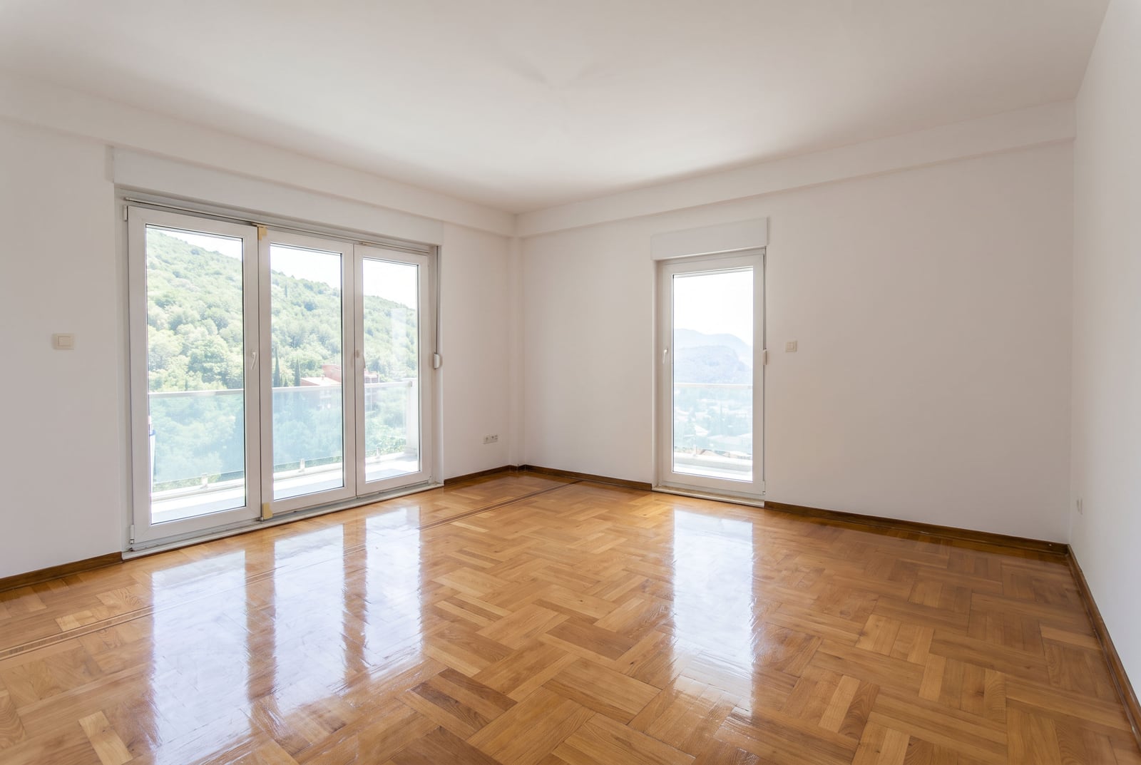 Bright empty bedroom with parquet flooring, panoramic windows, and a mountain view in Petrovac, Montenegro