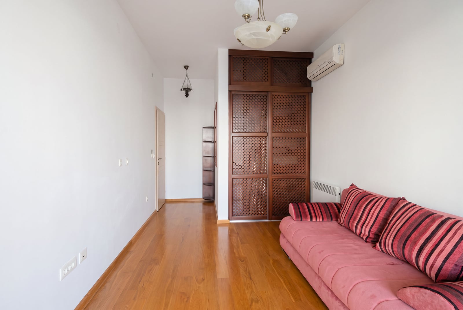 Living room with parquet flooring, a red sofa, and a wooden cabinet in an apartment in Bečići, Montenegro