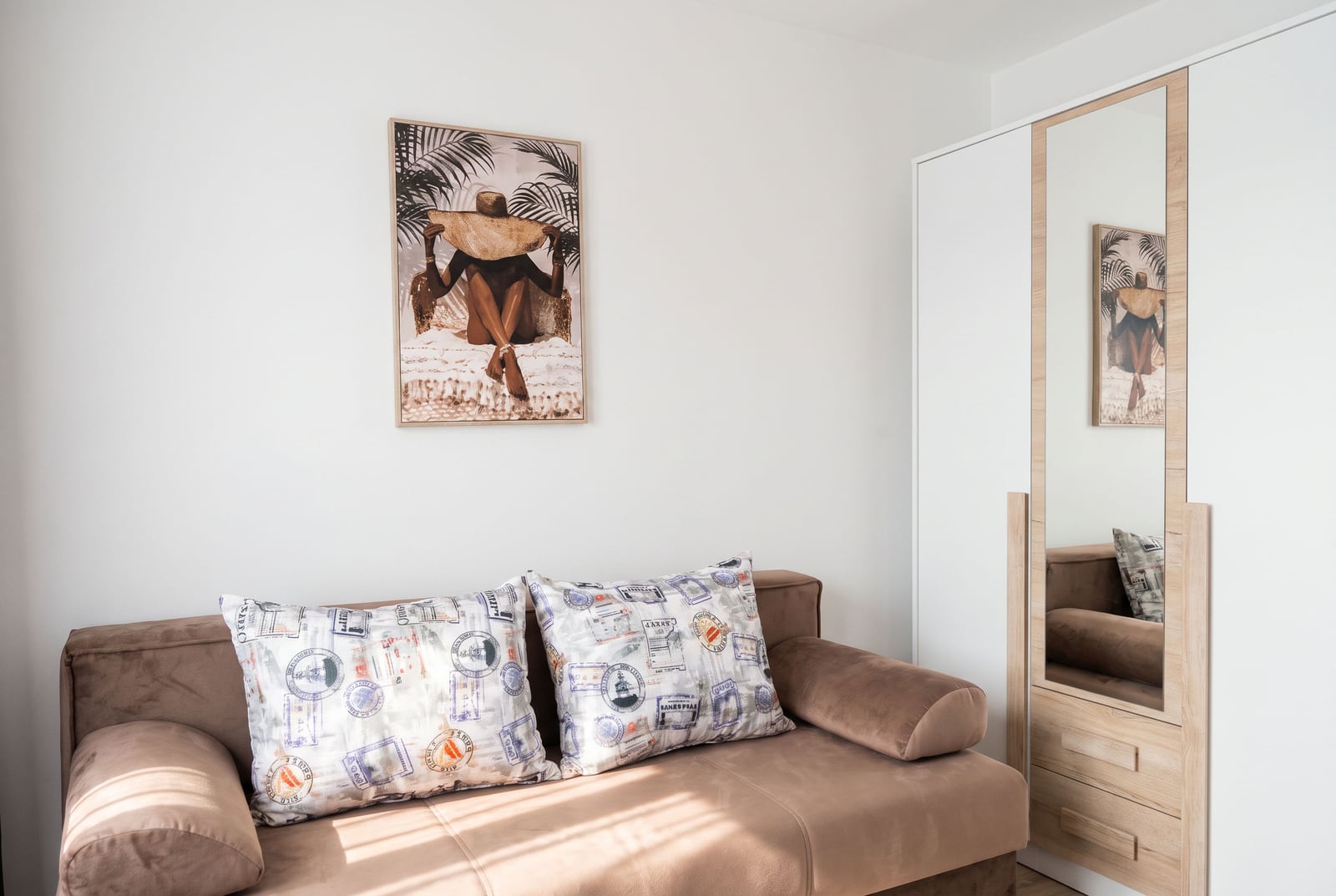 Brown sofa with pillows and a light wardrobe with a mirror in the bedroom of an apartment in Bečići, Montenegro.