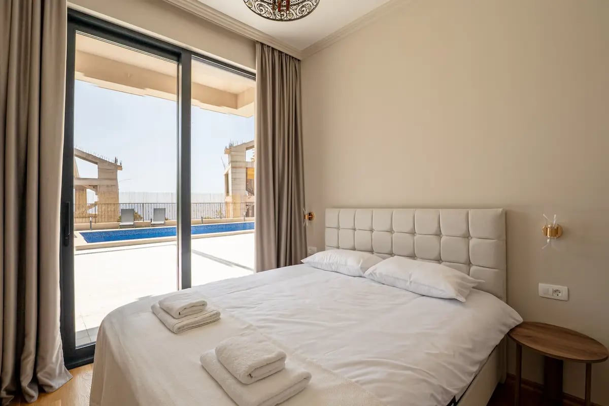 Chambre dans une villa à Reževići, Monténégro : lit double, baies vitrées avec accès à la piscine et à la terrasse.